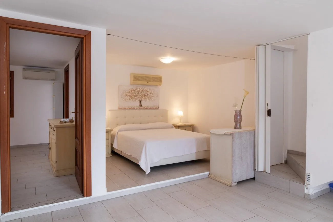 Se ve un dormitorio con una cama y mesitas de noche a través de una puerta abierta.
