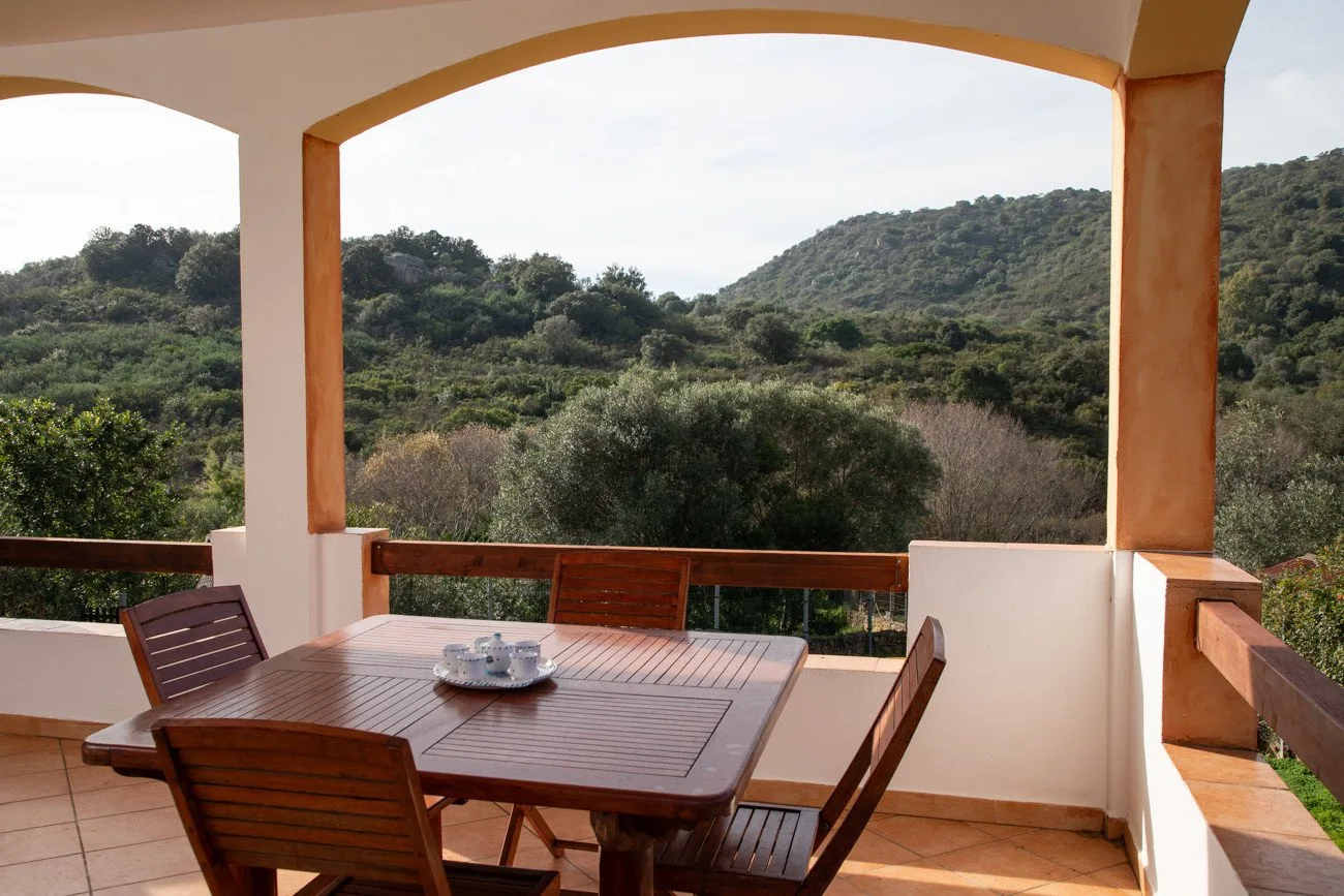 Una terraza cubierta con una mesa de comedor de madera frente a colinas verdes.