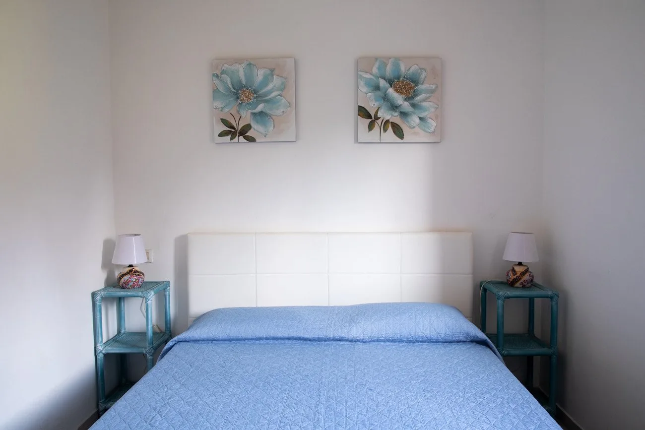 A bedroom with a blue bedspread and two floral pictures above the bed.