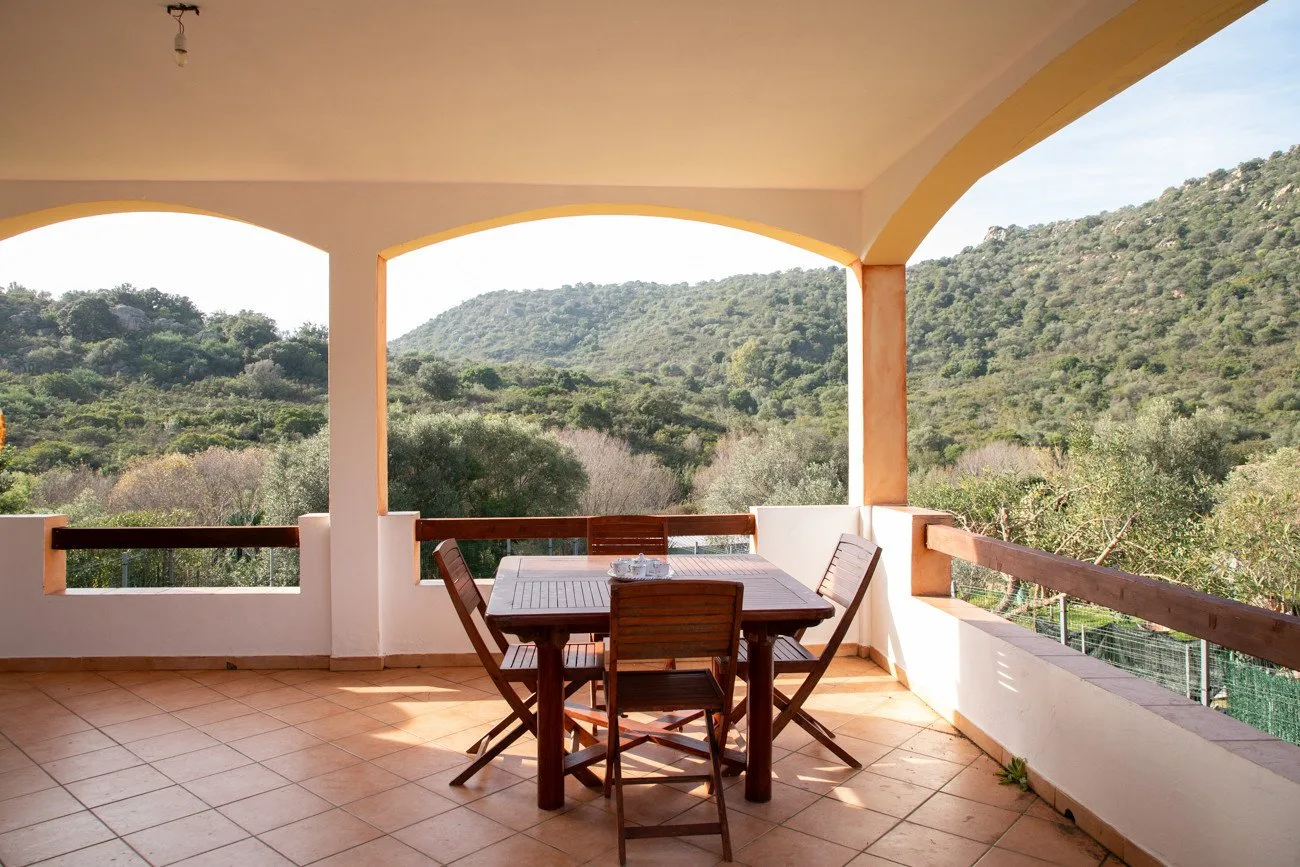 Una terraza cubierta tiene una mesa de comedor y sillas con vistas a colinas verdes.
