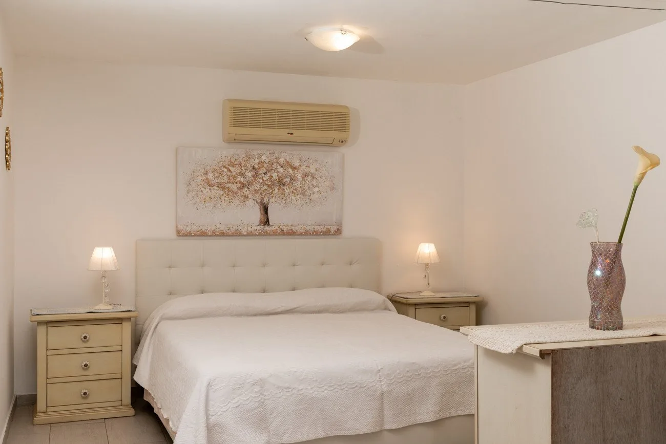 A bedroom with a bed, bedside tables, and a framed tree picture.
