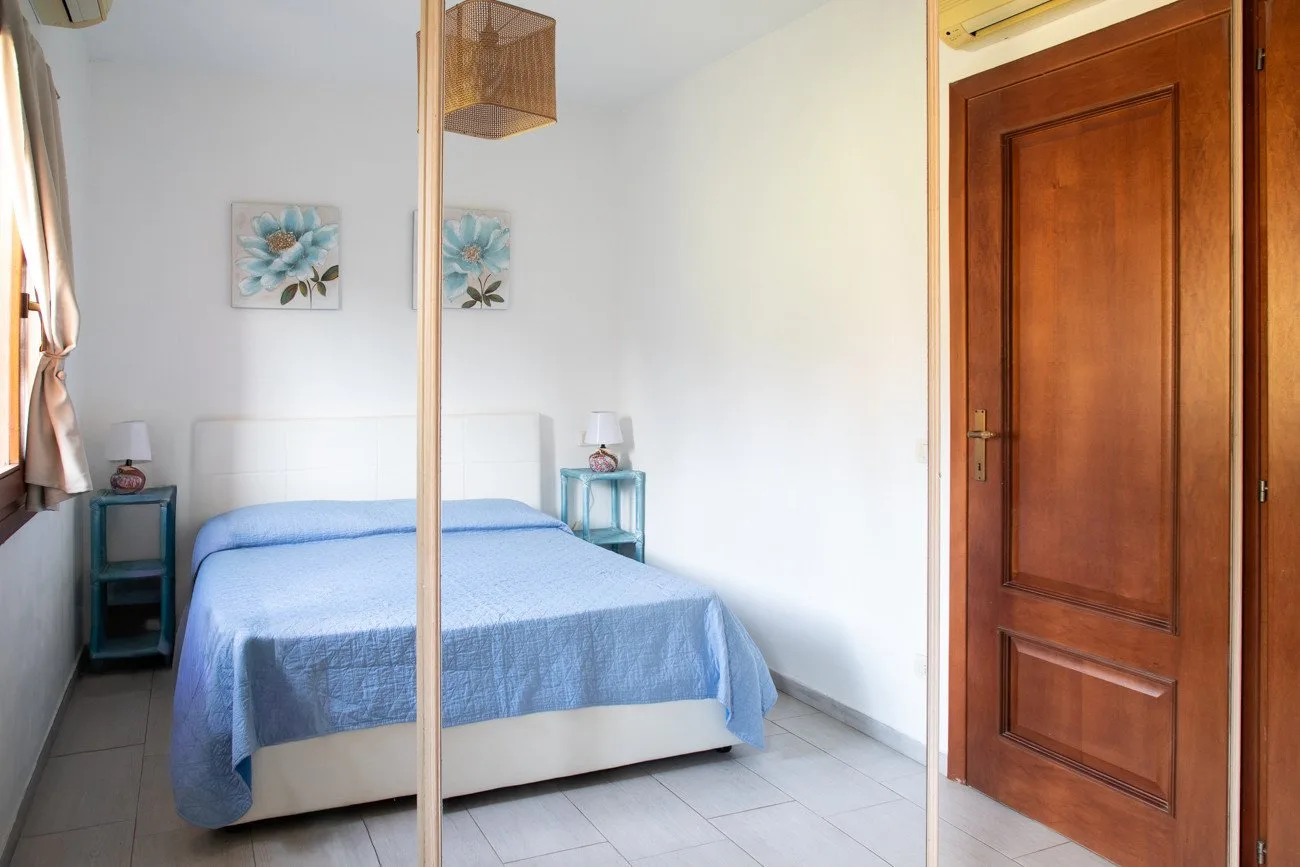 A bedroom with a blue-covered bed, bedside tables, and a wooden door.