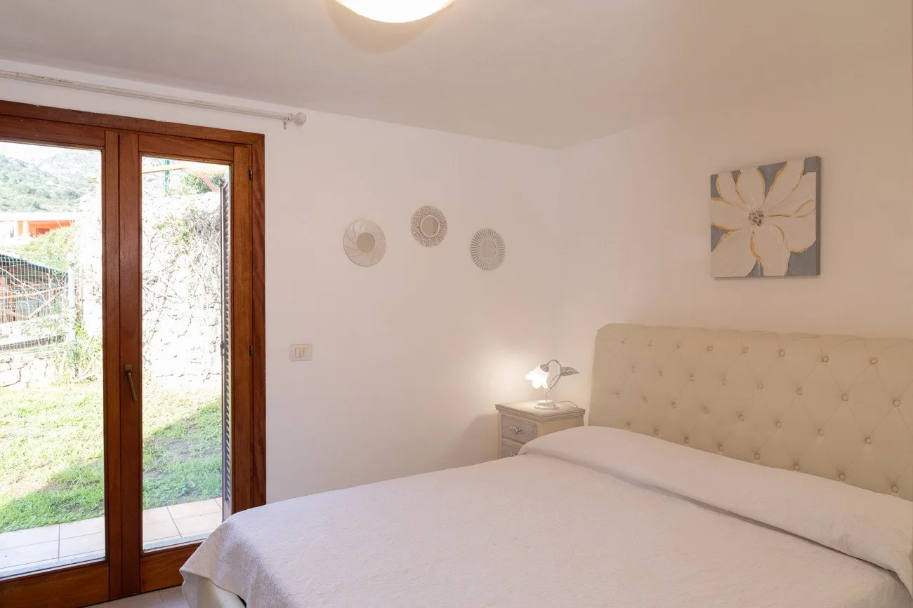A bedroom with a bed beside a glass door opening onto a garden.