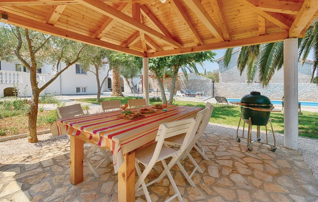 A covered outdoor dining area with a long table and a barbecue grill.