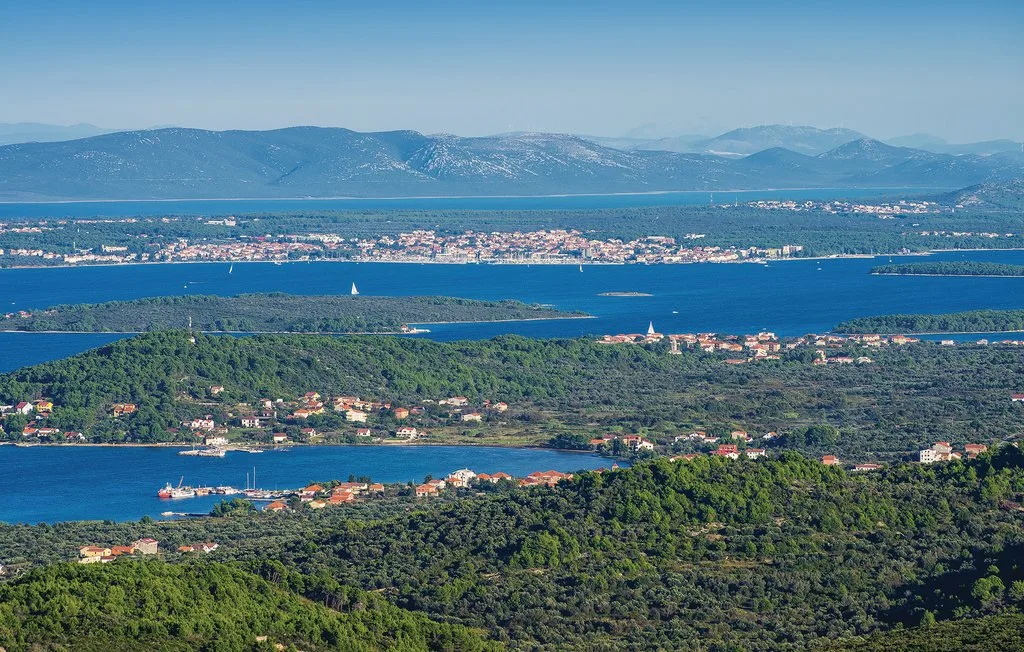 A coastal landscape with wooded hills, blue water, and distant mountains.