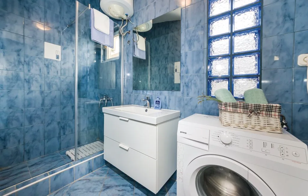 A blue-tiled bathroom with a shower, sink, and washing machine.
