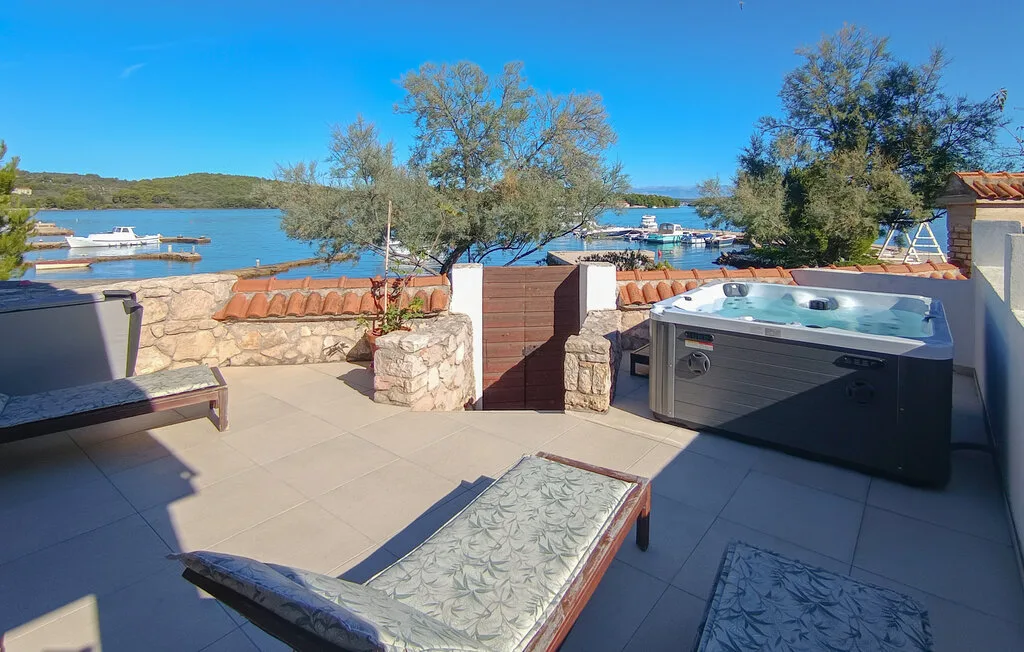 A tiled outdoor terrace overlooks the water, with a hot tub and lounge seating.