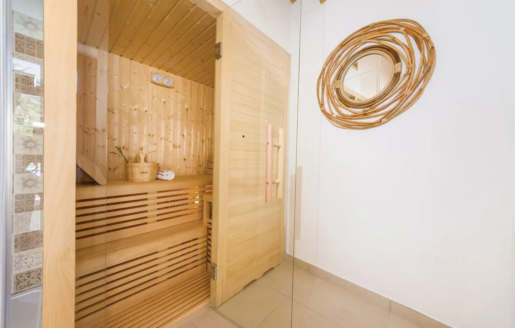 A wooden sauna with a slatted bench stands beside a white wall.
