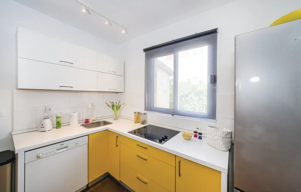 A bright kitchen with yellow cabinets, a cooktop, and a window.