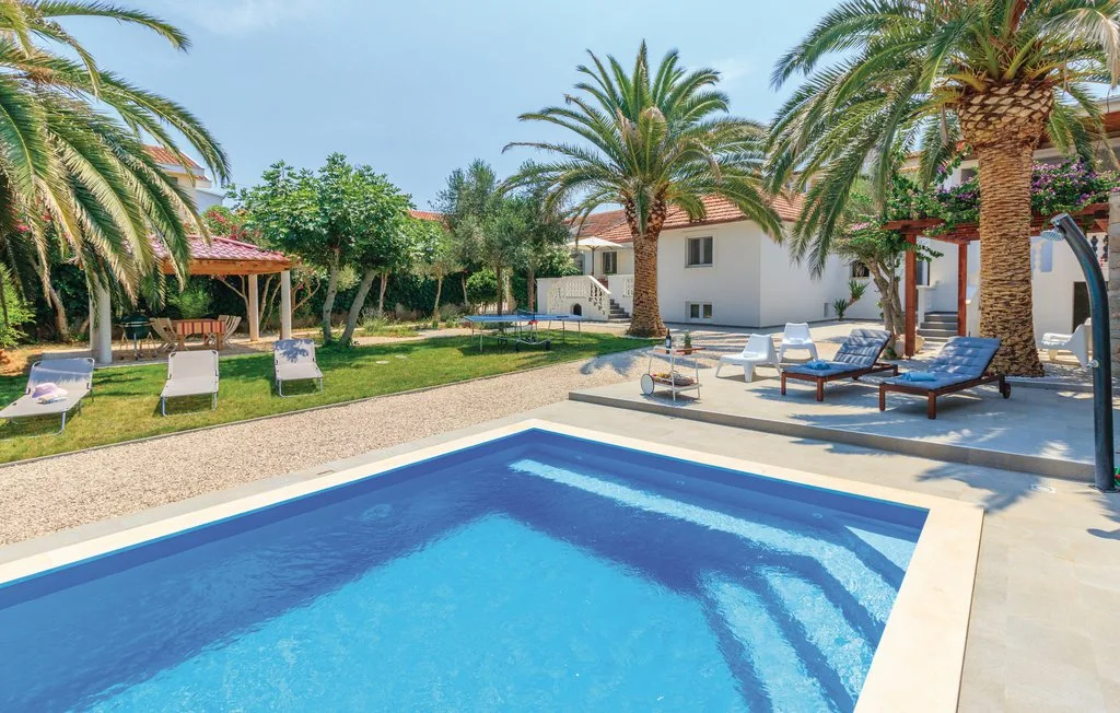 A swimming pool sits beside a landscaped garden and a white building.