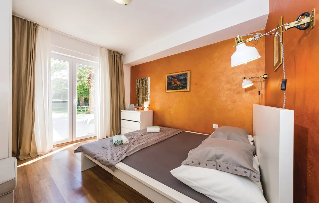 A bedroom with a bed beside a large window and orange accent wall.