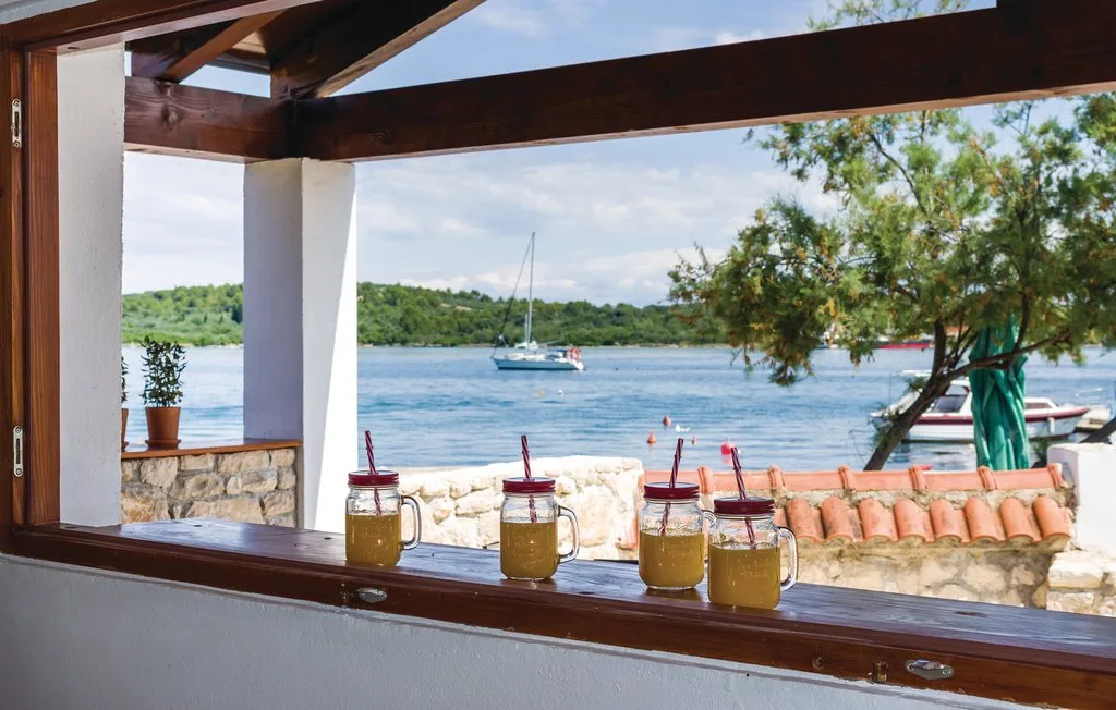 A waterfront patio frames a sailboat on the water, with drinks on the ledge.