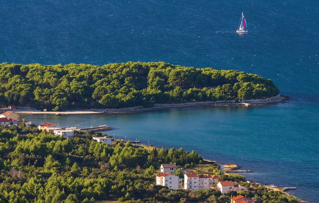 A coastal bay curves around a wooded peninsula, with buildings along the shore.