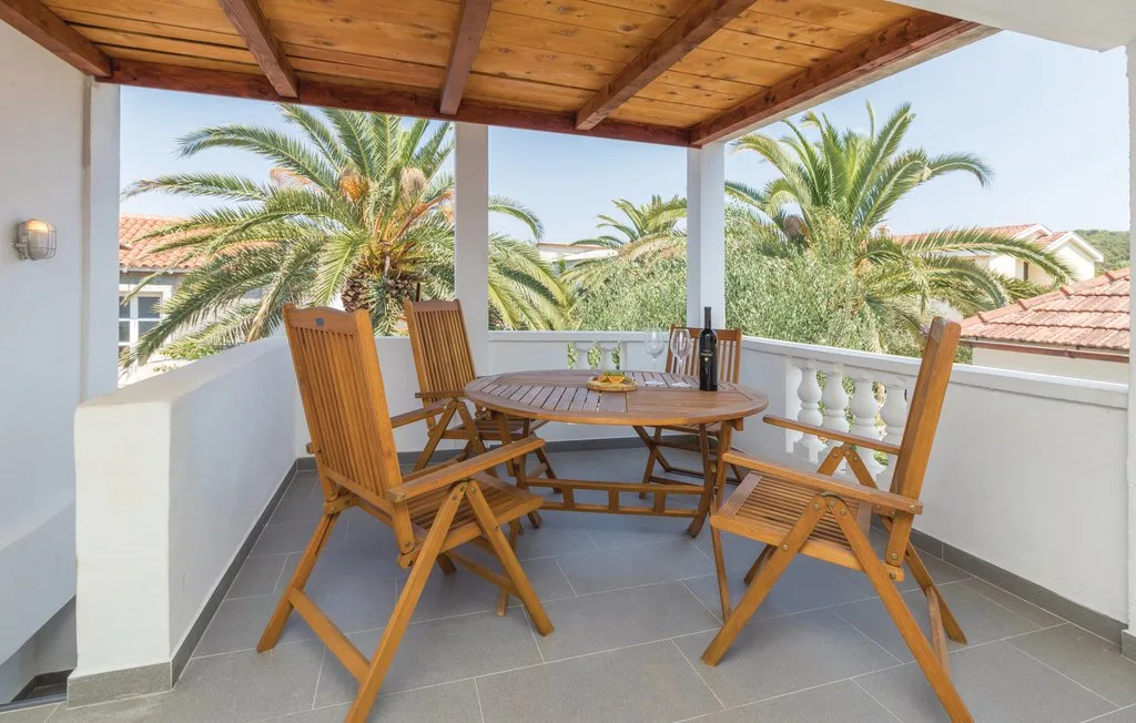 A covered terrace with wooden seating and a table overlooks palm trees.