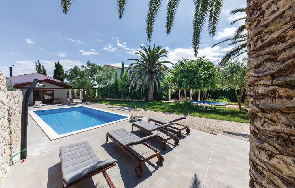 An outdoor pool area with lounge seating, greenery, and a small trampoline.