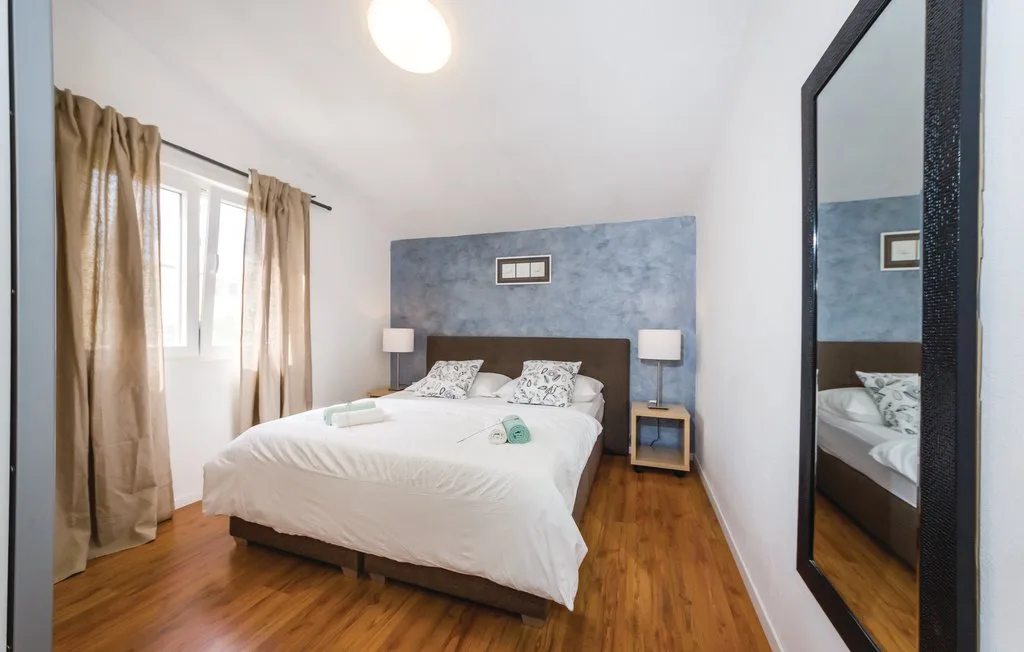 A bedroom with a bed against a blue accent wall and a window with curtains.