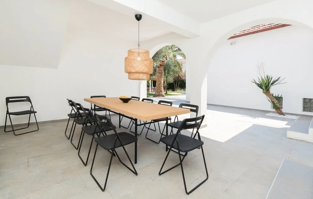 A bright dining area has a long table, folding chairs, and an arched opening.