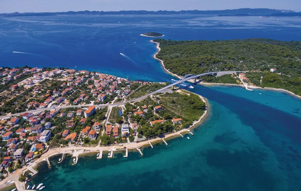 Aerial view of a coastal settlement beside a bridge crossing a turquoise channel.