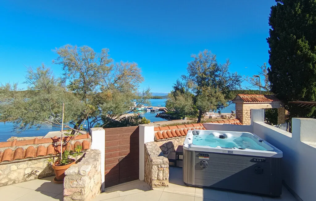 An outdoor terrace with a hot tub overlooks a lake beneath a clear blue sky.