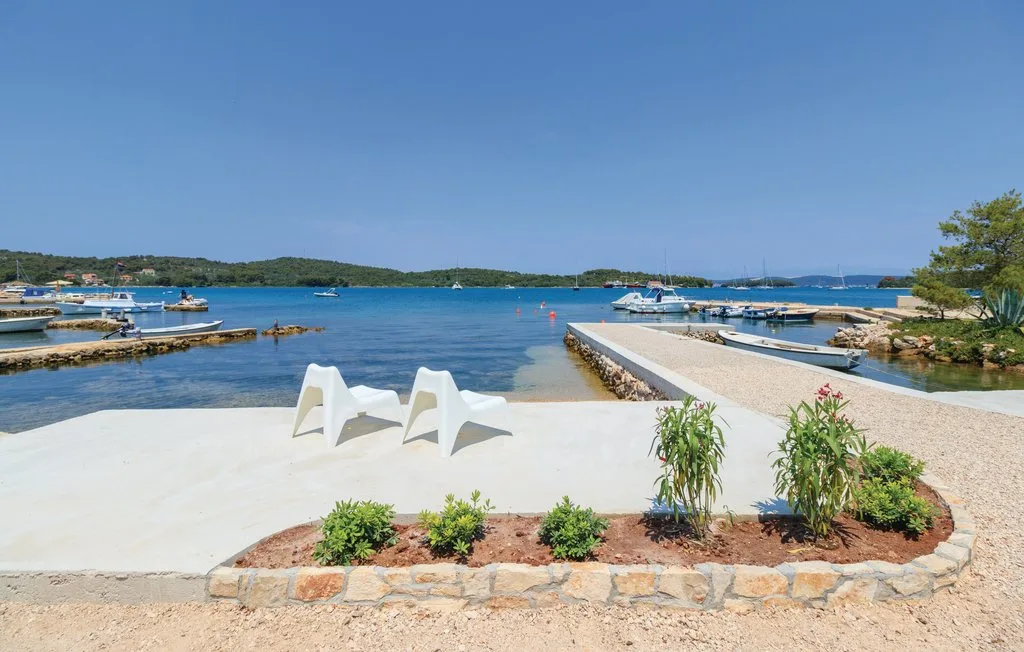 A waterfront terrace with white seating overlooks calm blue water and moored boats.