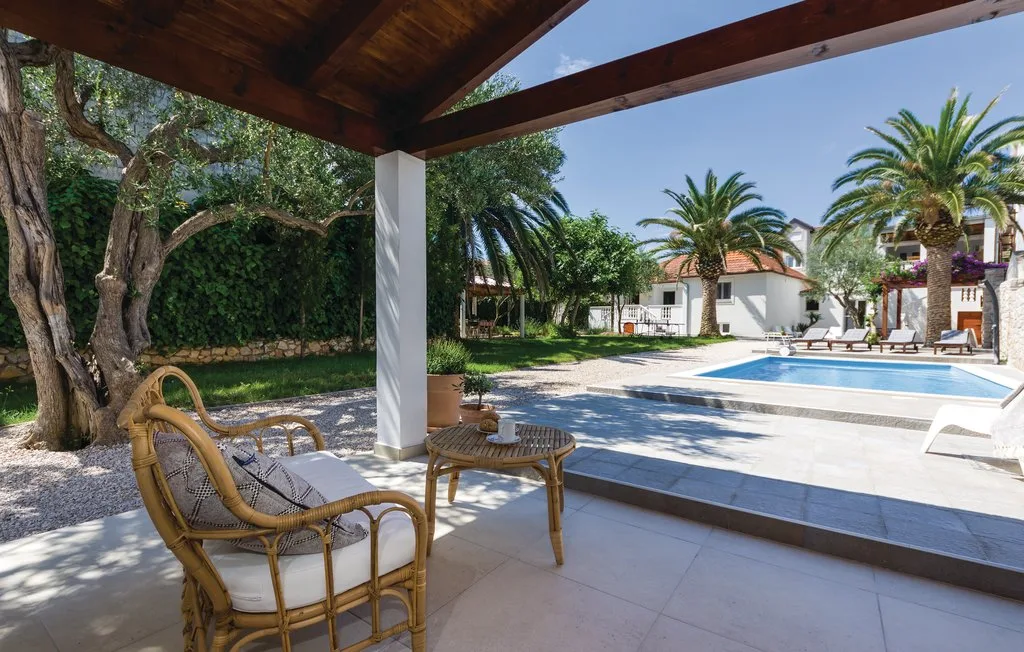 A shaded patio with wicker seating overlooks a swimming pool and palm trees.