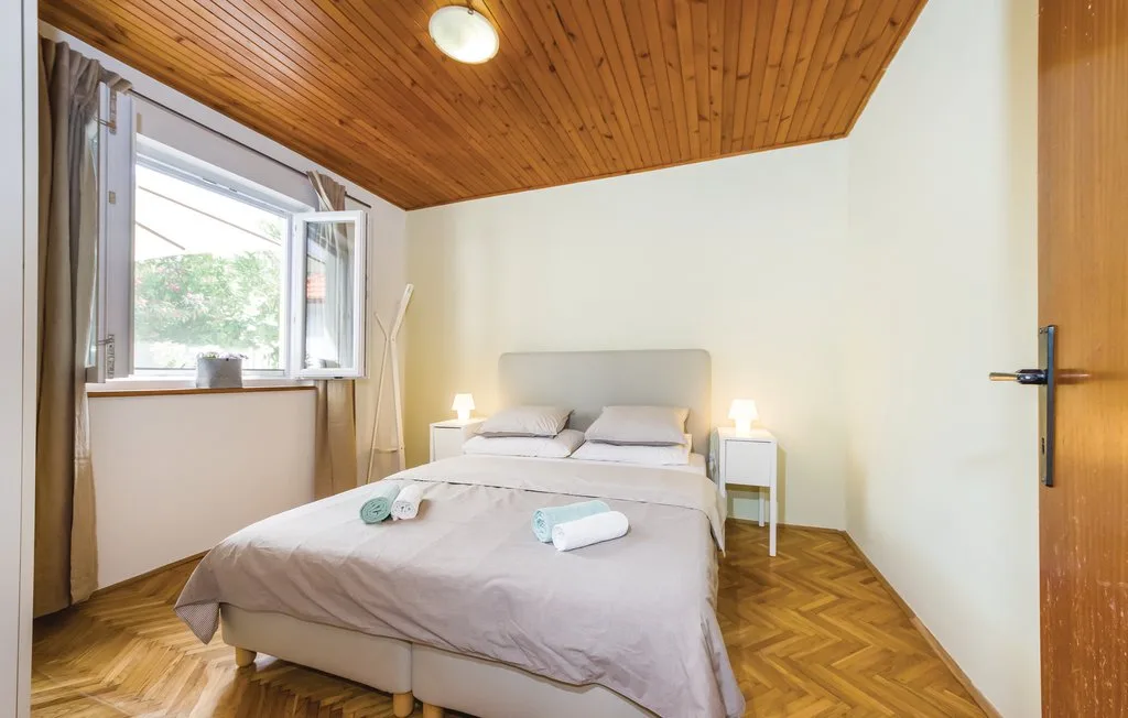 A bedroom with a bed beneath a sloped wooden ceiling and an open window.