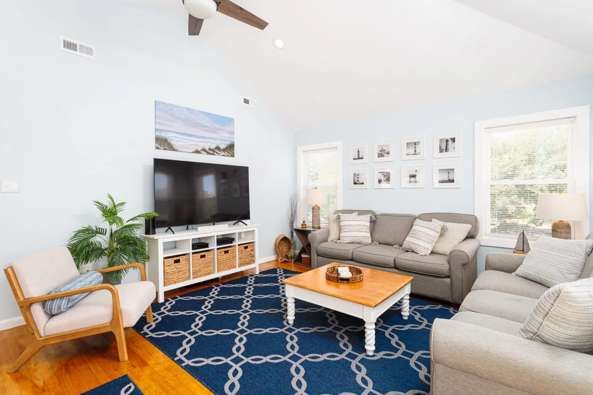 Una sala luminosa con un sofá gris, un televisor y una alfombra azul estampada.