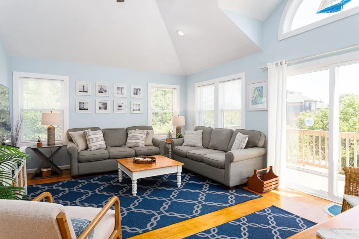 Una sala luminosa con asientos grises, una alfombra azul estampada y ventanas grandes.