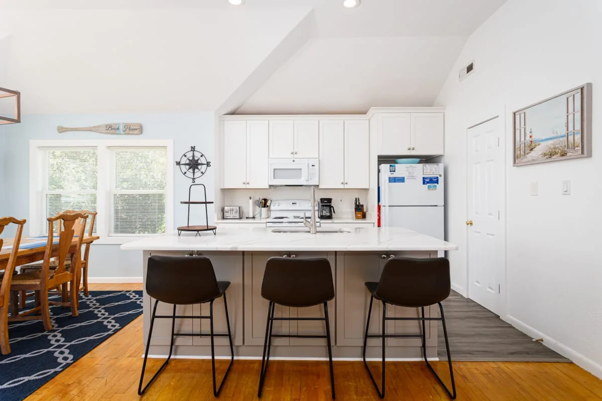 Una cocina luminosa con una isla central y asientos, junto a un comedor.