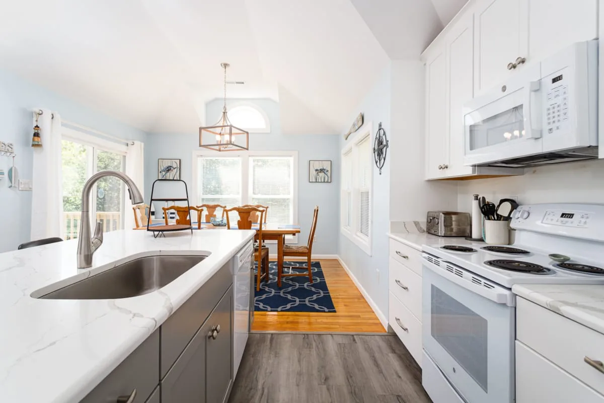 Una cocina luminosa con una isla blanca y una mesa de comedor junto a las ventanas.