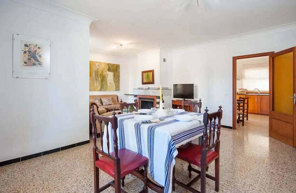 Un comedor con una mesa larga preparada y una zona de estar al fondo.