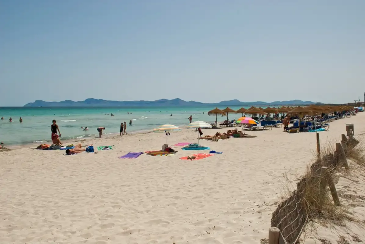 Una playa de arena con bañistas en el agua y sombrillas junto a la orilla.