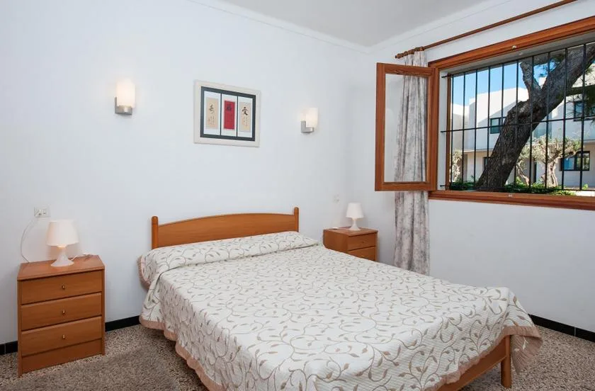 Un dormitorio con cama doble, mesitas de madera y una ventana abierta.