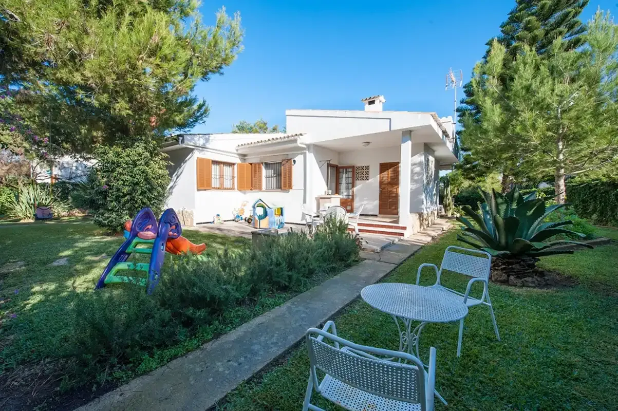 Una casa blanca da a un patio ajardinado con asientos al aire libre.