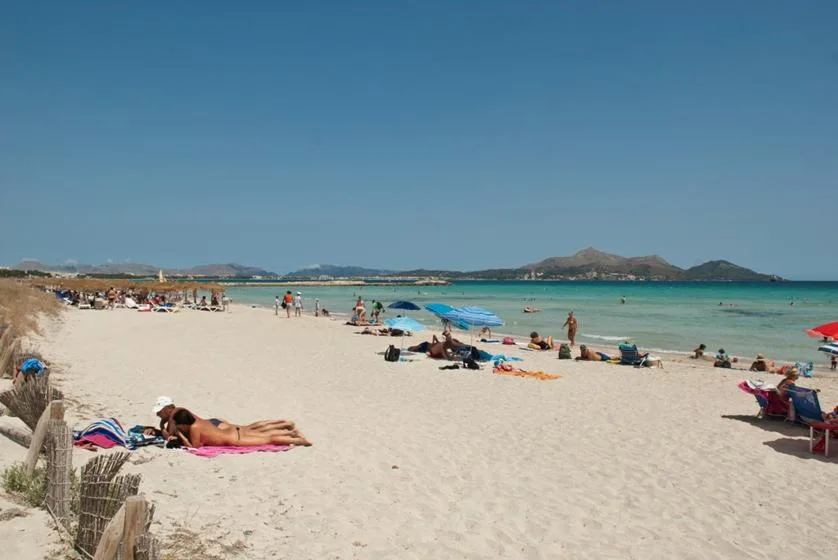 Una playa de arena con bañistas y agua turquesa bajo un cielo despejado.