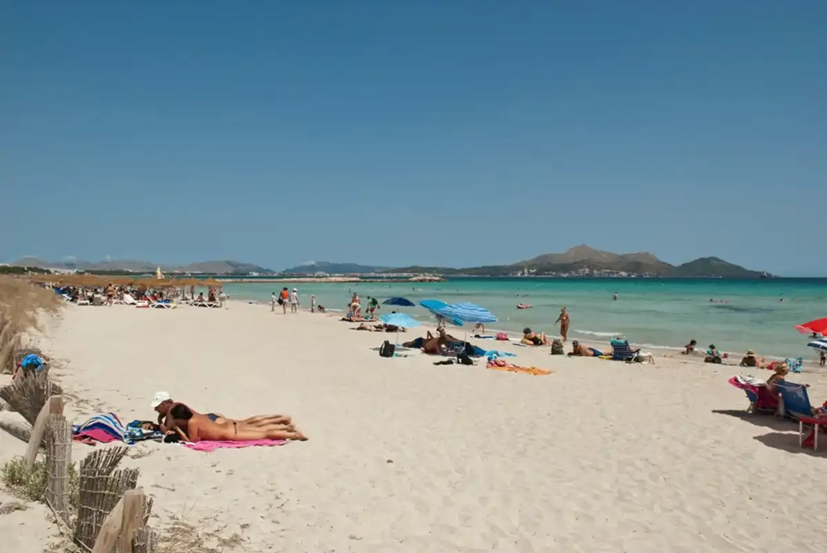 Una playa de arena con bañistas y agua turquesa junto a la orilla.