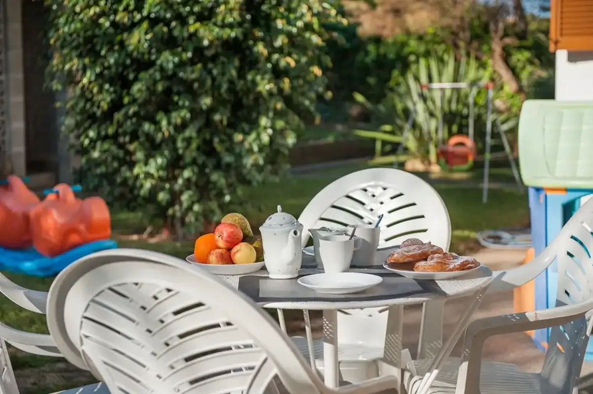 Comedor exterior en un patio con una mesa, sillas blancas y fruta.