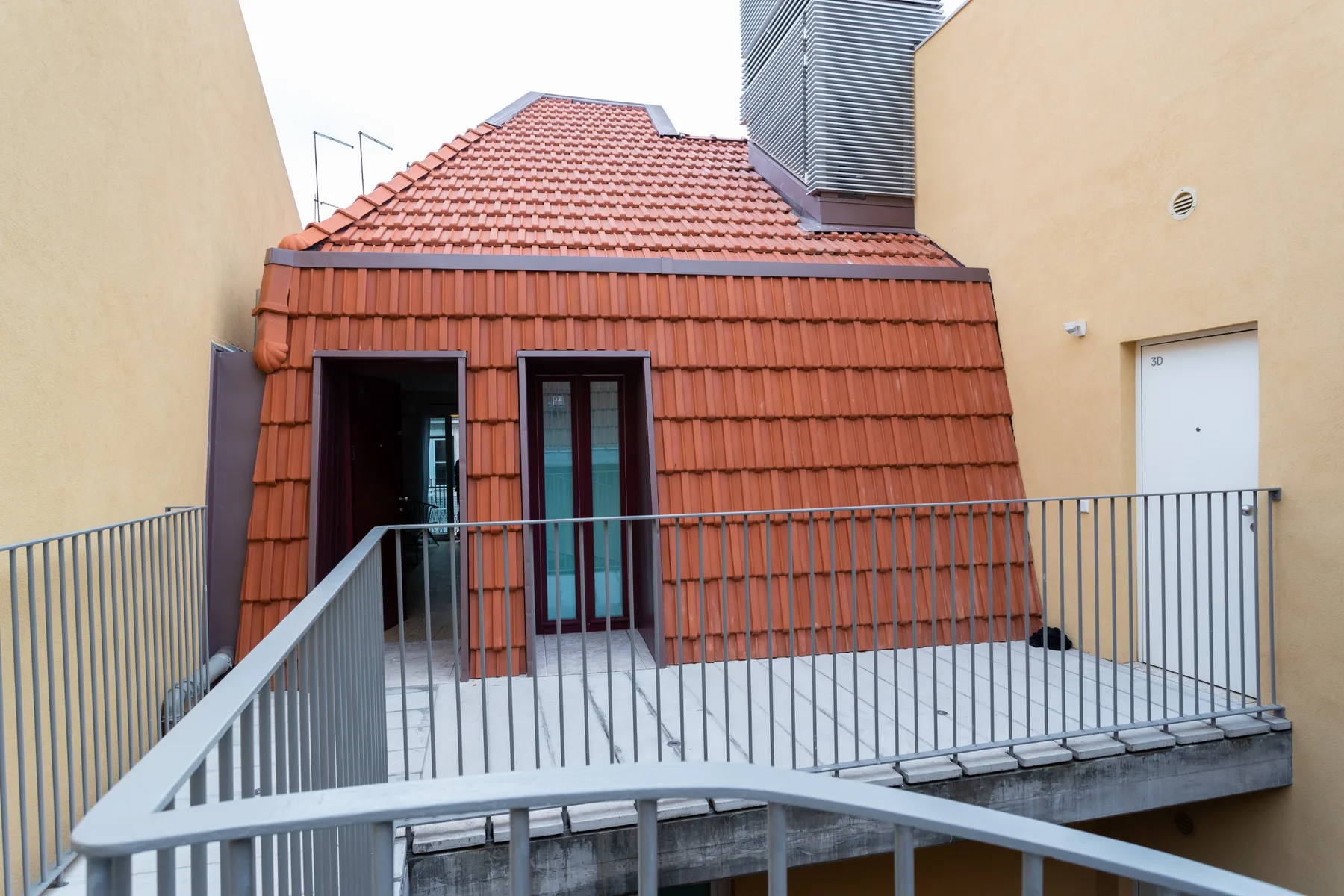 An exterior terrace with metal railings sits beside a red-tiled roof.