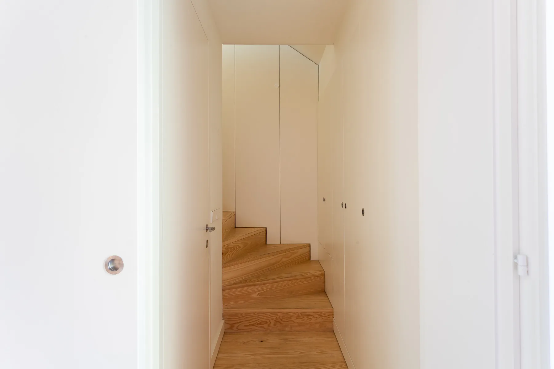 A narrow indoor staircase with wooden steps leads upward between white walls.