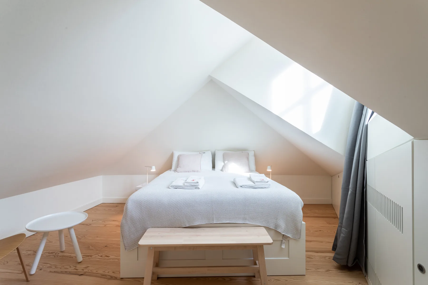 A bedroom with a double bed beneath a sloped ceiling and skylight.