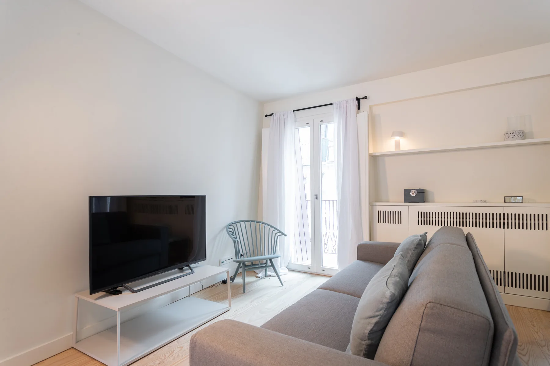A bright living room with a television, seating, and tall curtained windows.