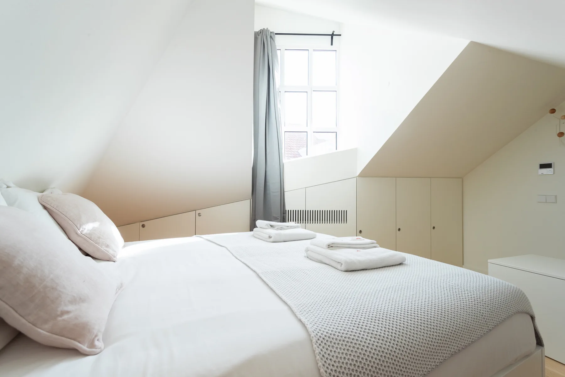 A bright bedroom with a white bed beneath a sloped ceiling.