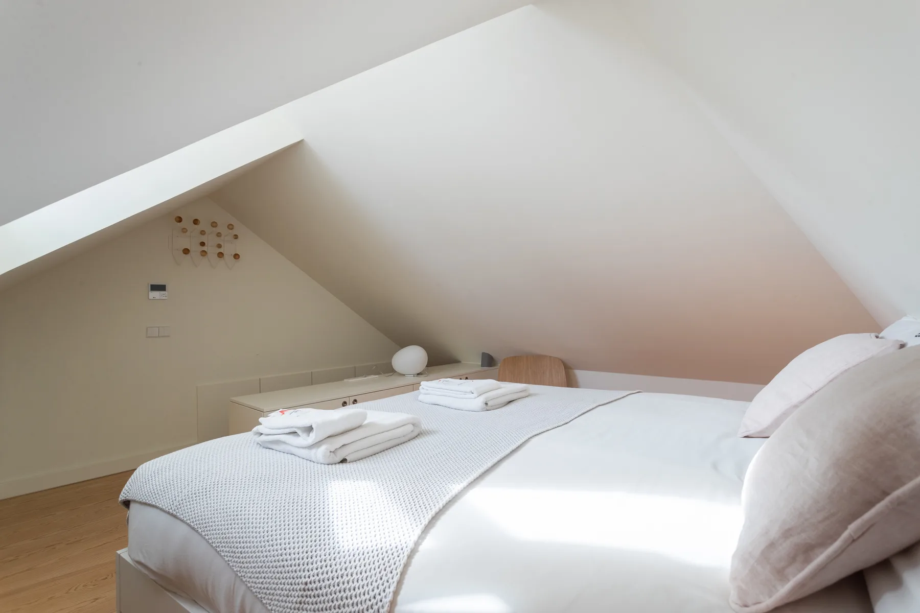 A bright bedroom with two beds beneath a sloped ceiling.