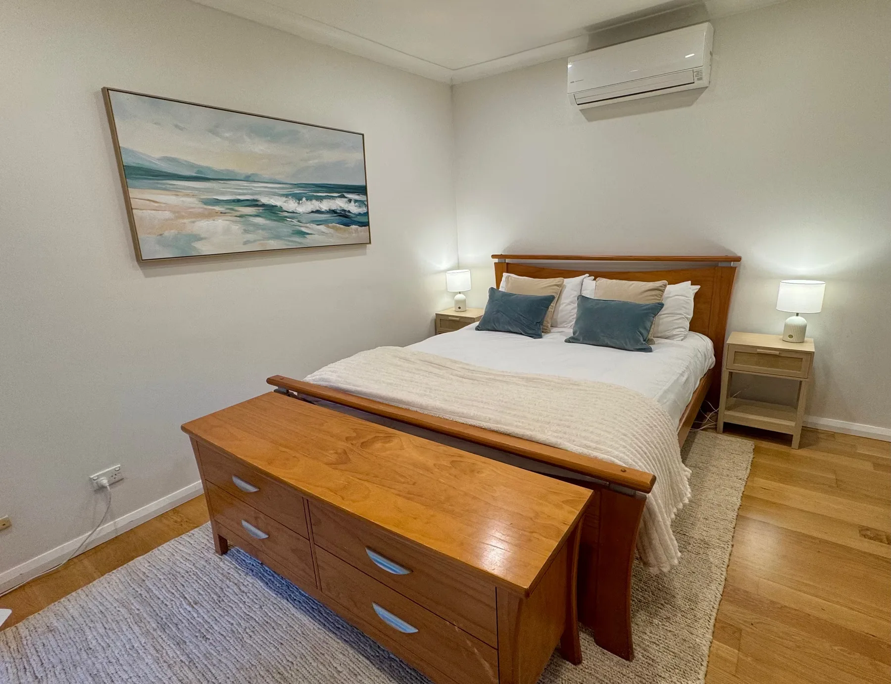 A bedroom with a bed, wooden dresser, and framed ocean artwork.
