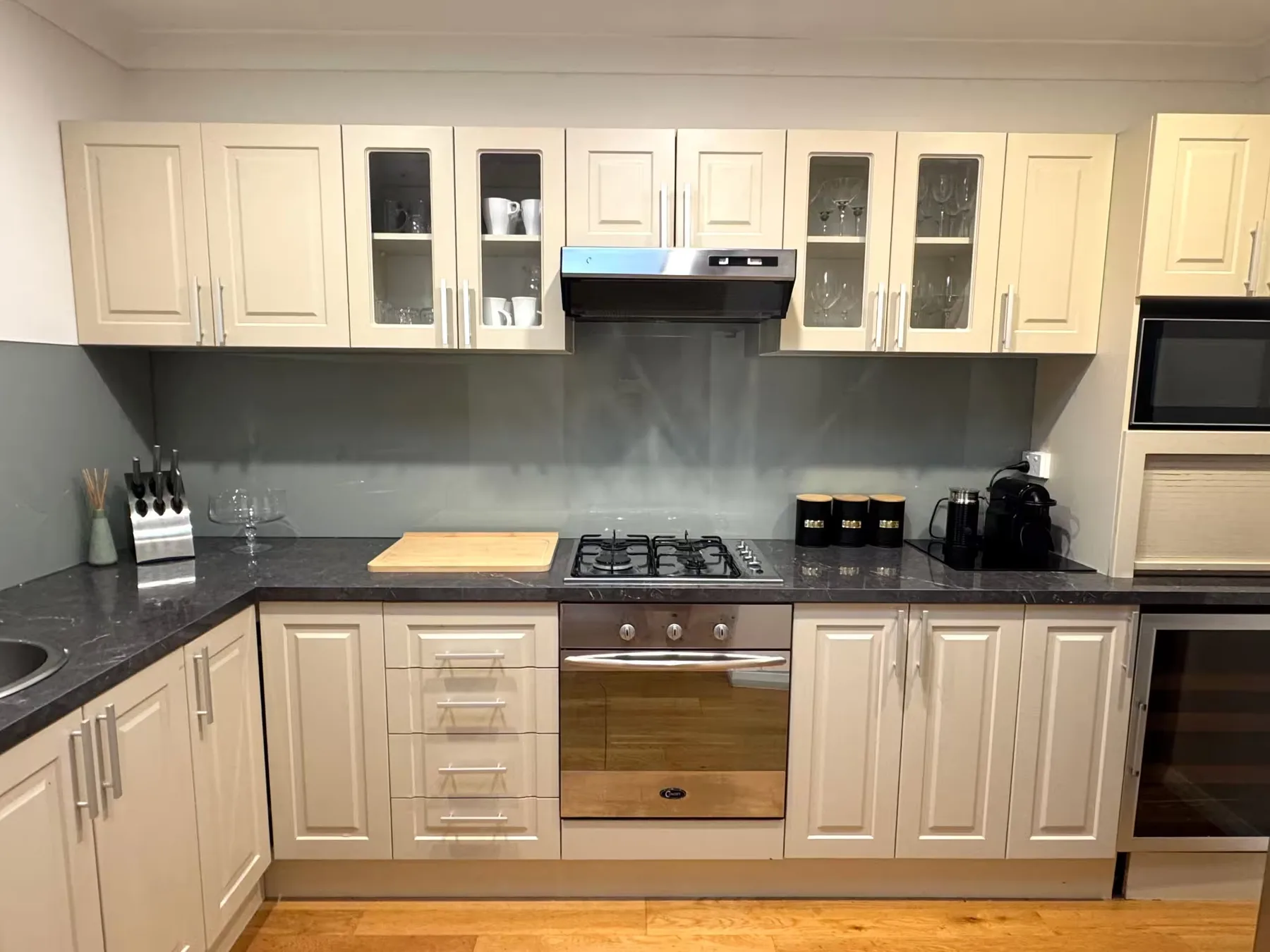 A modern kitchen with pale cabinets, dark counters, and a built-in oven.