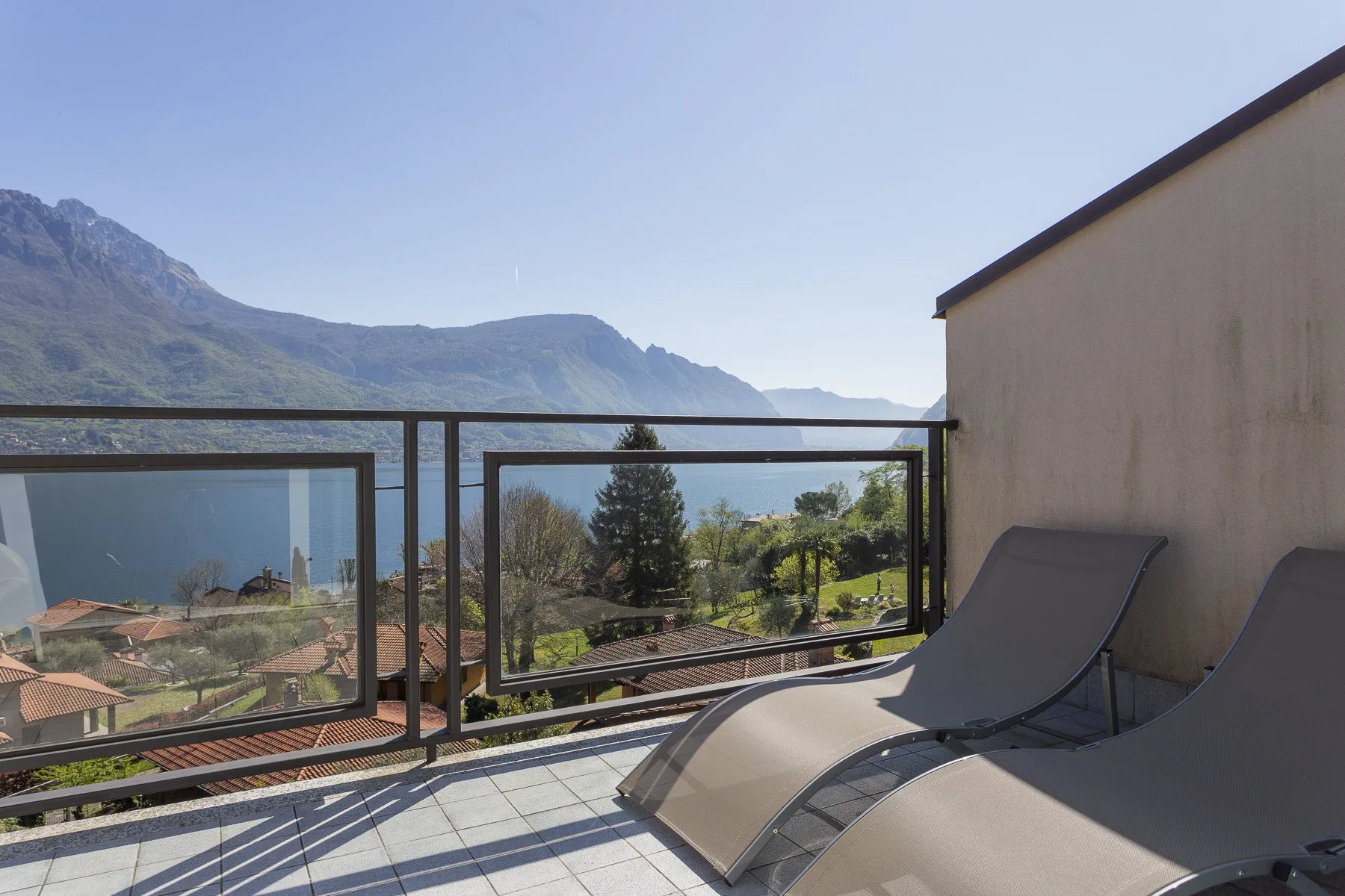 A tiled outdoor terrace with reclining lounge chairs overlooks a mountain landscape.
