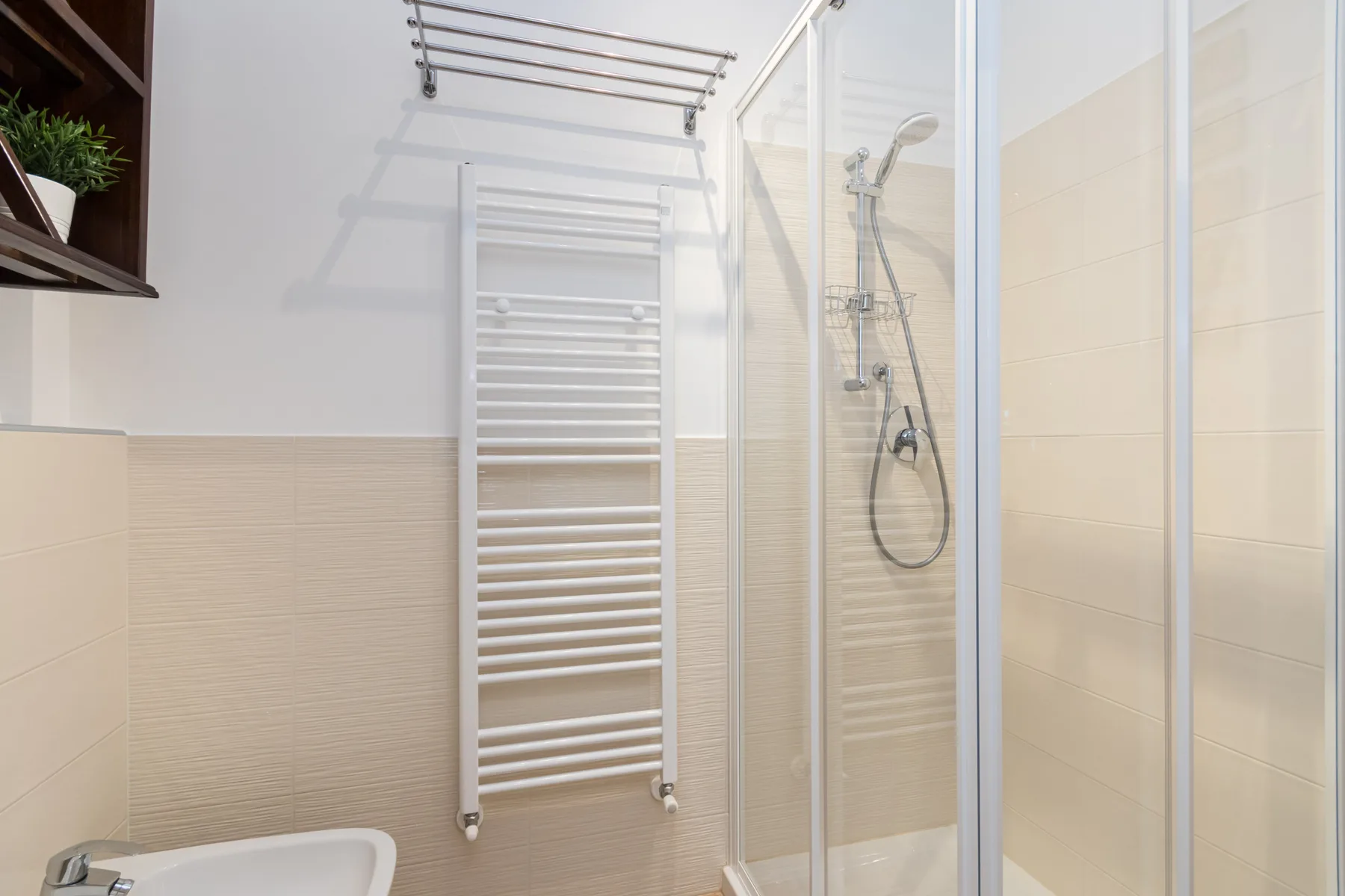 Un baño luminoso con una ducha de cristal y un toallero calefactable en la pared.
