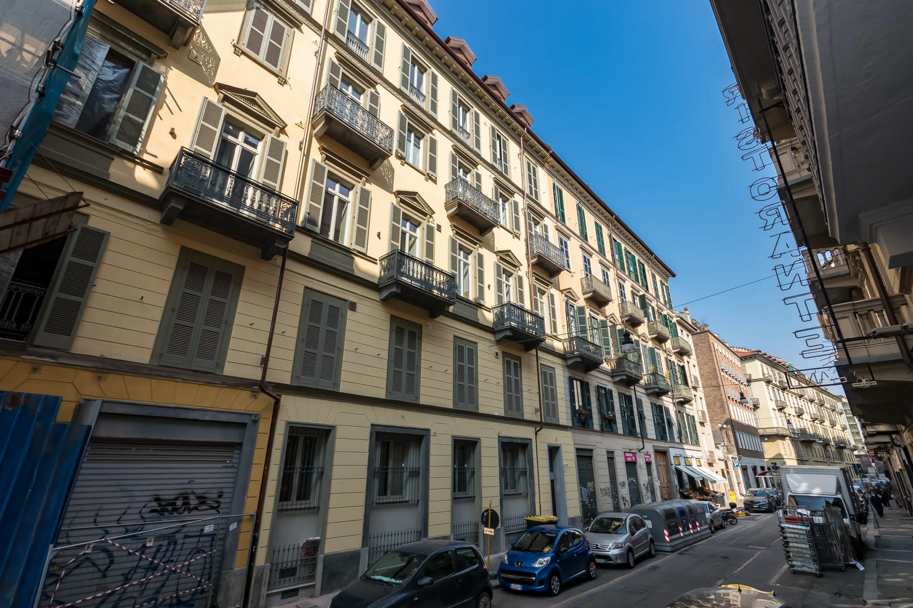 Una calle urbana bordeada de edificios de varias plantas y coches estacionados.