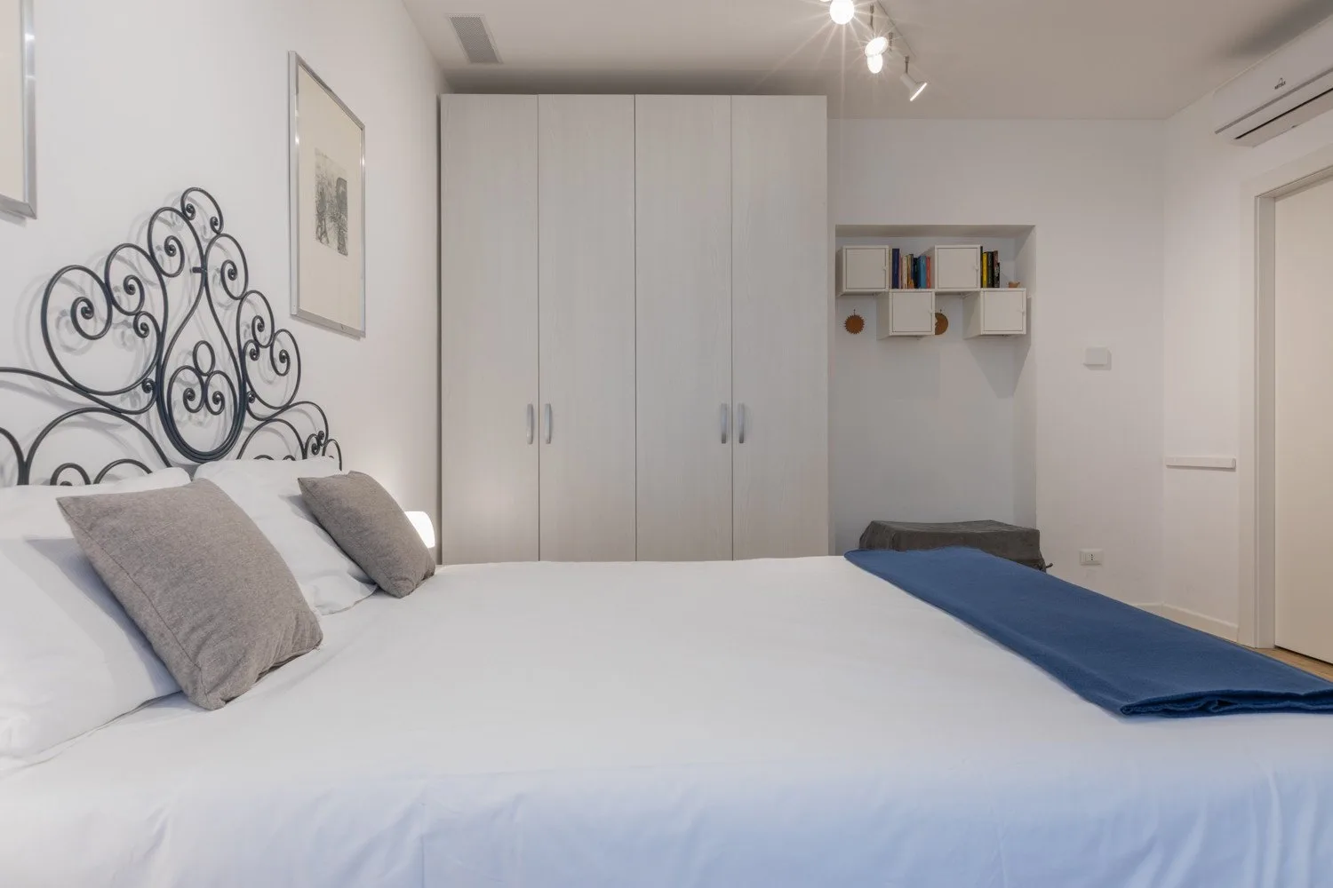 A bedroom with a large bed, a white wardrobe, and a small wall shelf.