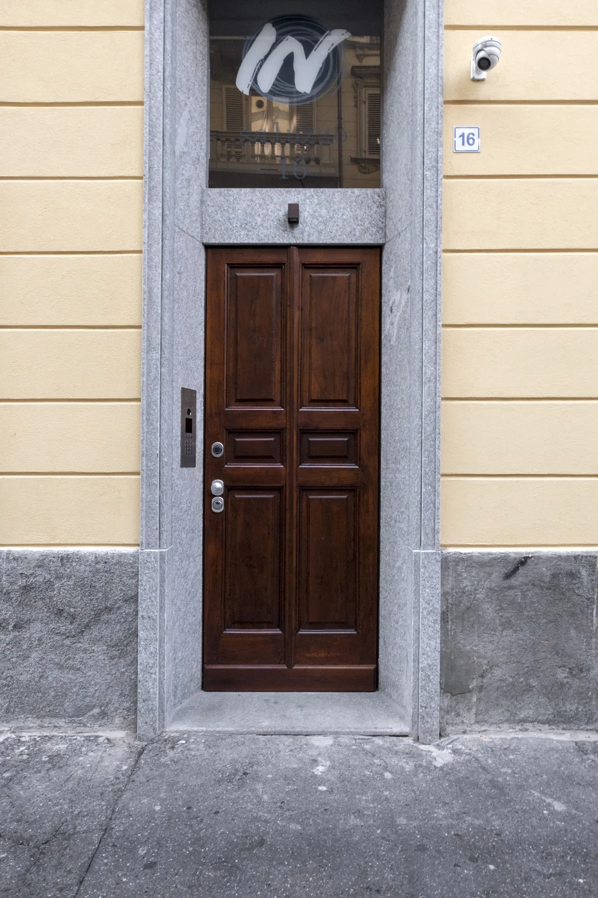Una puerta de entrada de madera oscura enmarcada en piedra sobre una fachada amarilla.